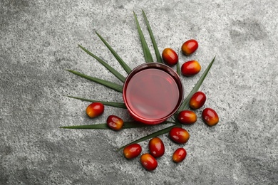 Palm oil in glass bowl, tropical leaf and fruits on grey table, flat lay