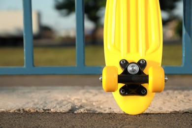 Photo of Modern yellow skateboard near fence outdoors, closeup. Space for text