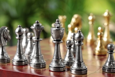 Golden and silver chess pieces on game board against blurred background, closeup