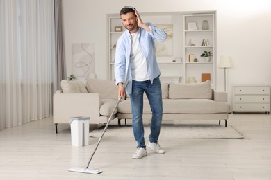 Photo of Enjoying cleaning. Man in headphones listening to music and mopping floor at home