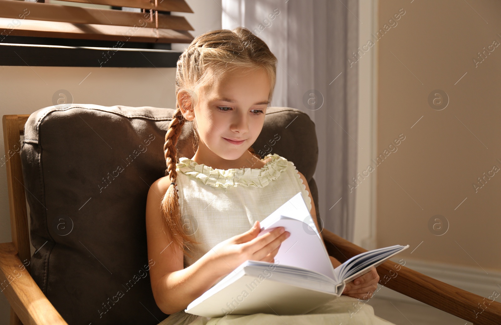 Photo of Little girl reading book in armchair at home