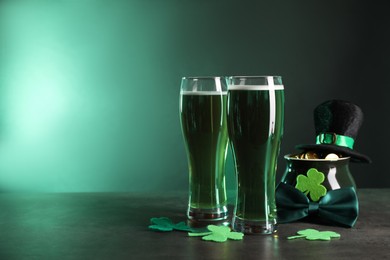 Photo of St. Patrick's day celebration. Green beer, leprechaun hat, pot of gold and decorative clover leaves on grey table. Space for text