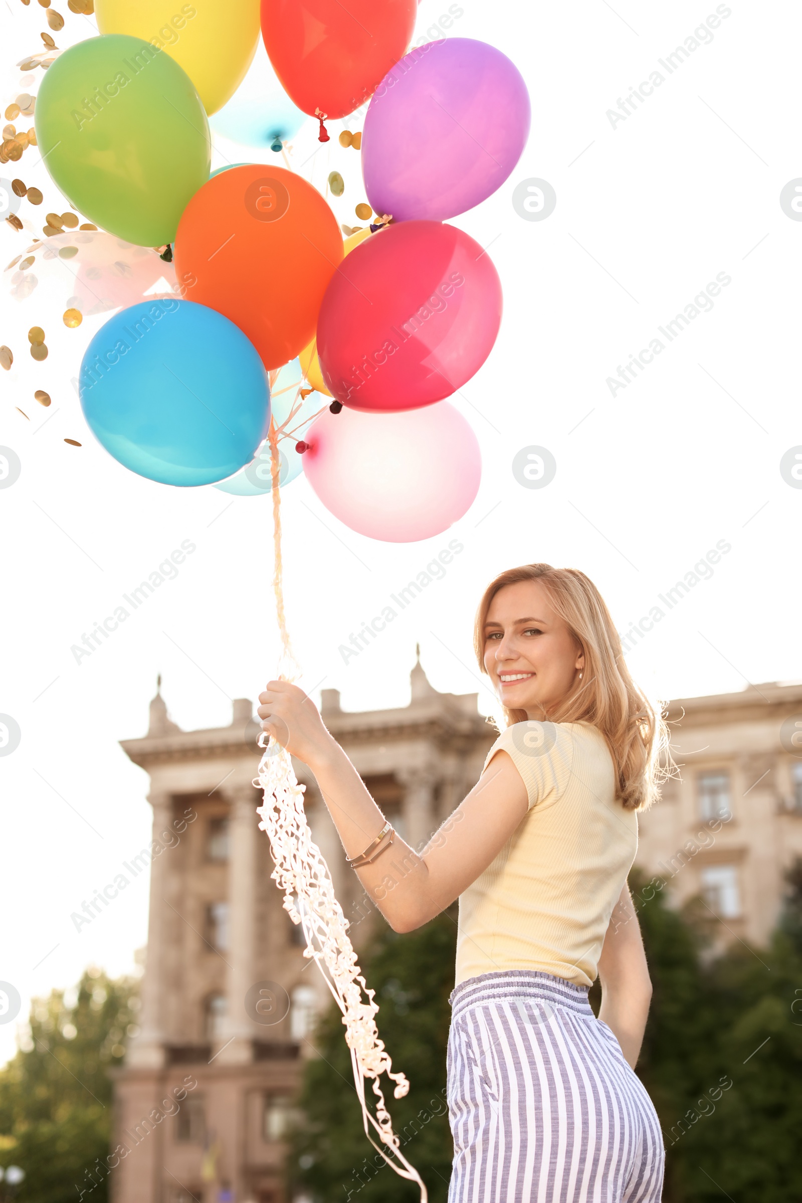 Photo of Young woman with colorful balloons outdoors on sunny day