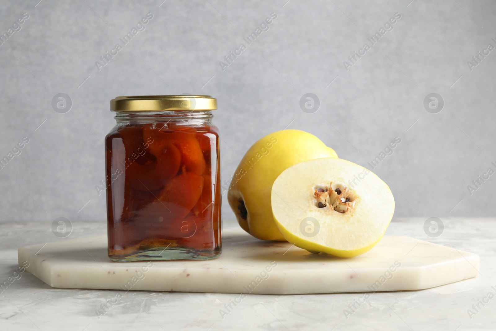 Photo of Tasty homemade quince jam in jar and fruits on grey textured table