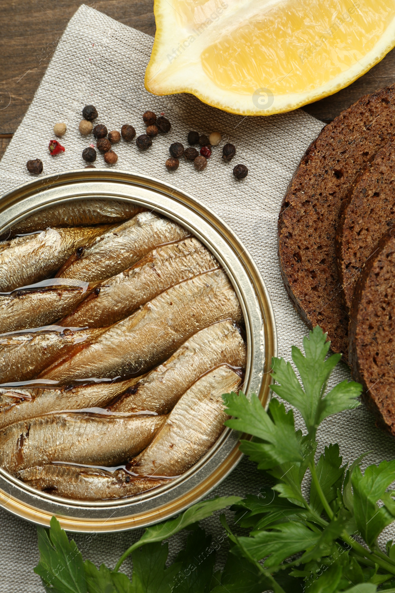 Photo of Tin can with tasty sprats served on wooden table, flat lay