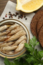 Tin can with tasty sprats served on wooden table, flat lay