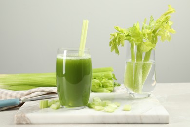 Glass of celery juice and fresh vegetables on light gray table