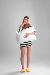 Photo of Young woman in pajamas with pillow on gray background