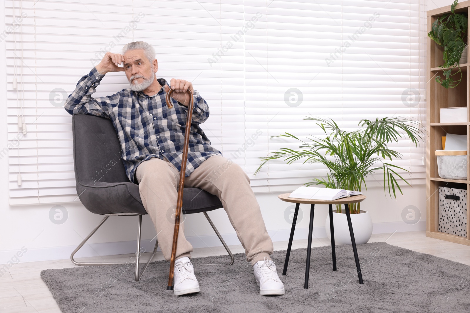 Photo of Senior man with walking cane sitting on armchair at home