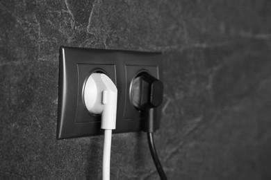 Power sockets with inserted plugs on dark grey wall, closeup. Electrical supply