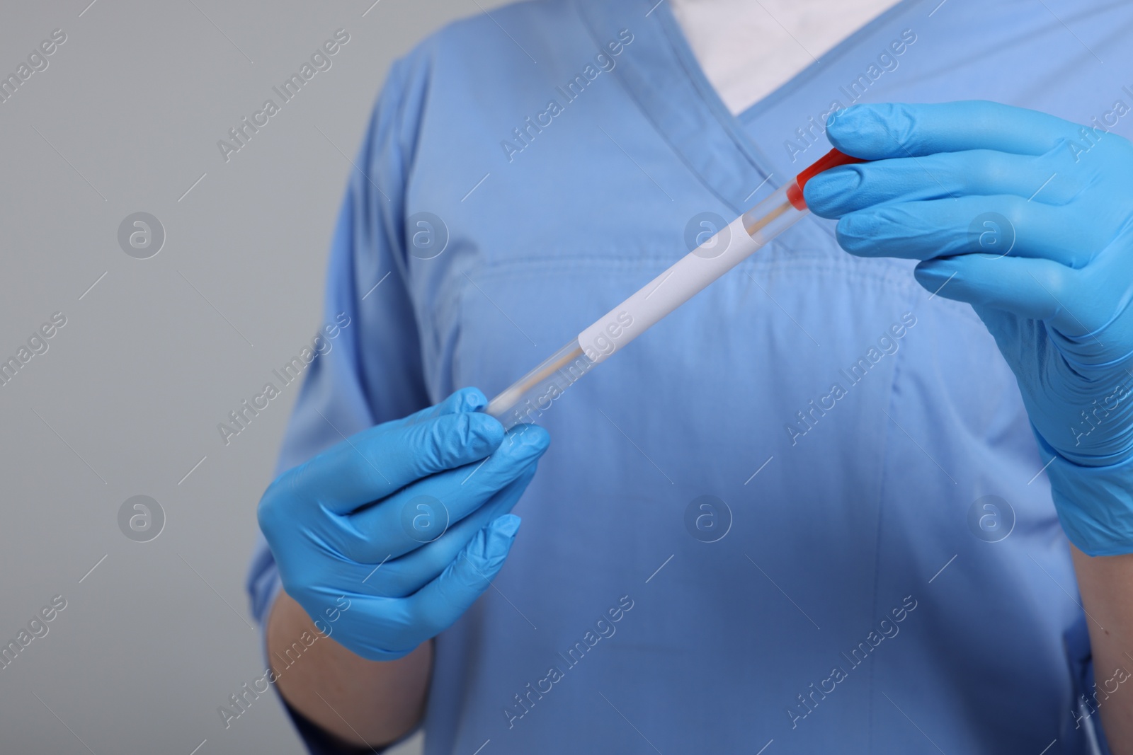 Photo of Laboratory testing. Doctor with cotton swab and tube on light grey background, closeup