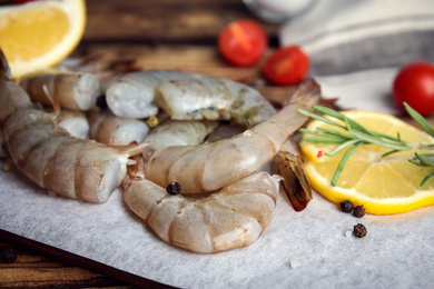 Photo of Fresh raw shrimps with lemon and rosemary on wooden board, closeup