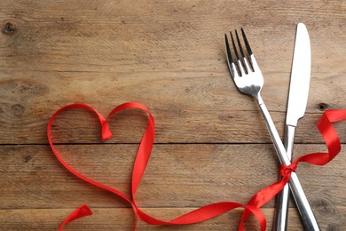 Photo of Cutlery set and red ribbon on wooden background, above view with space for text. Valentine's Day dinner