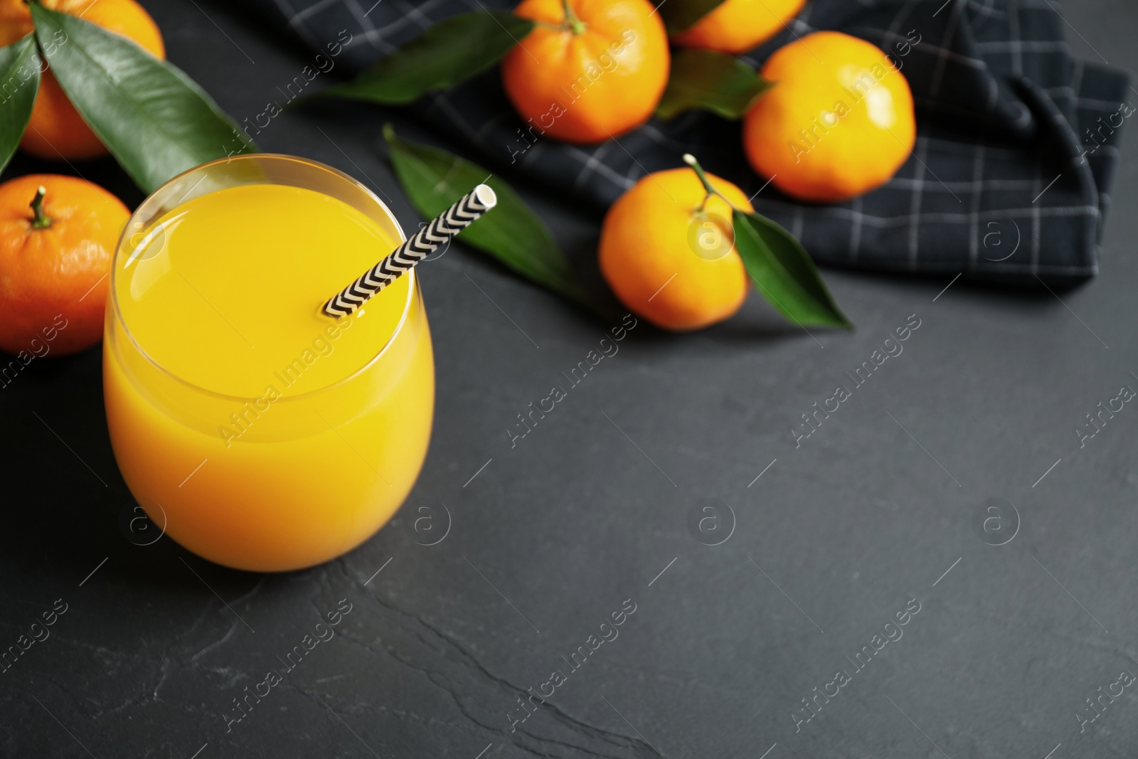 Photo of Glass of fresh tangerine juice and fruits on black table. Space for text