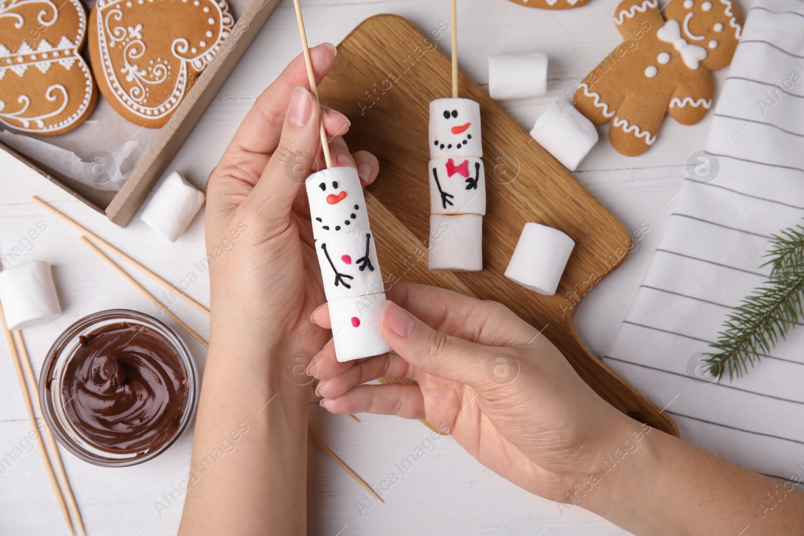 Photo of Woman making funny snowman with marshmallows at white wooden table, top view