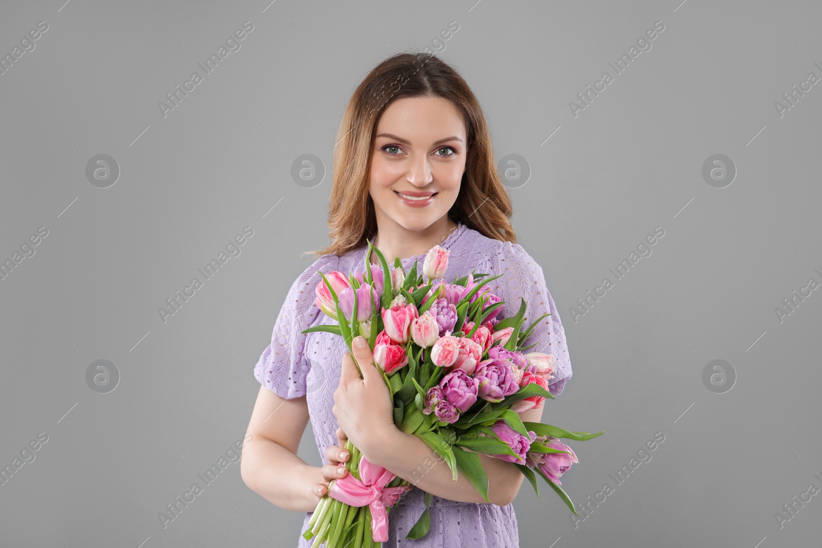 Photo of Happy young woman with bouquet of beautiful tulips on grey background