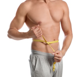 Young man with slim body using measuring tape on white background, closeup view