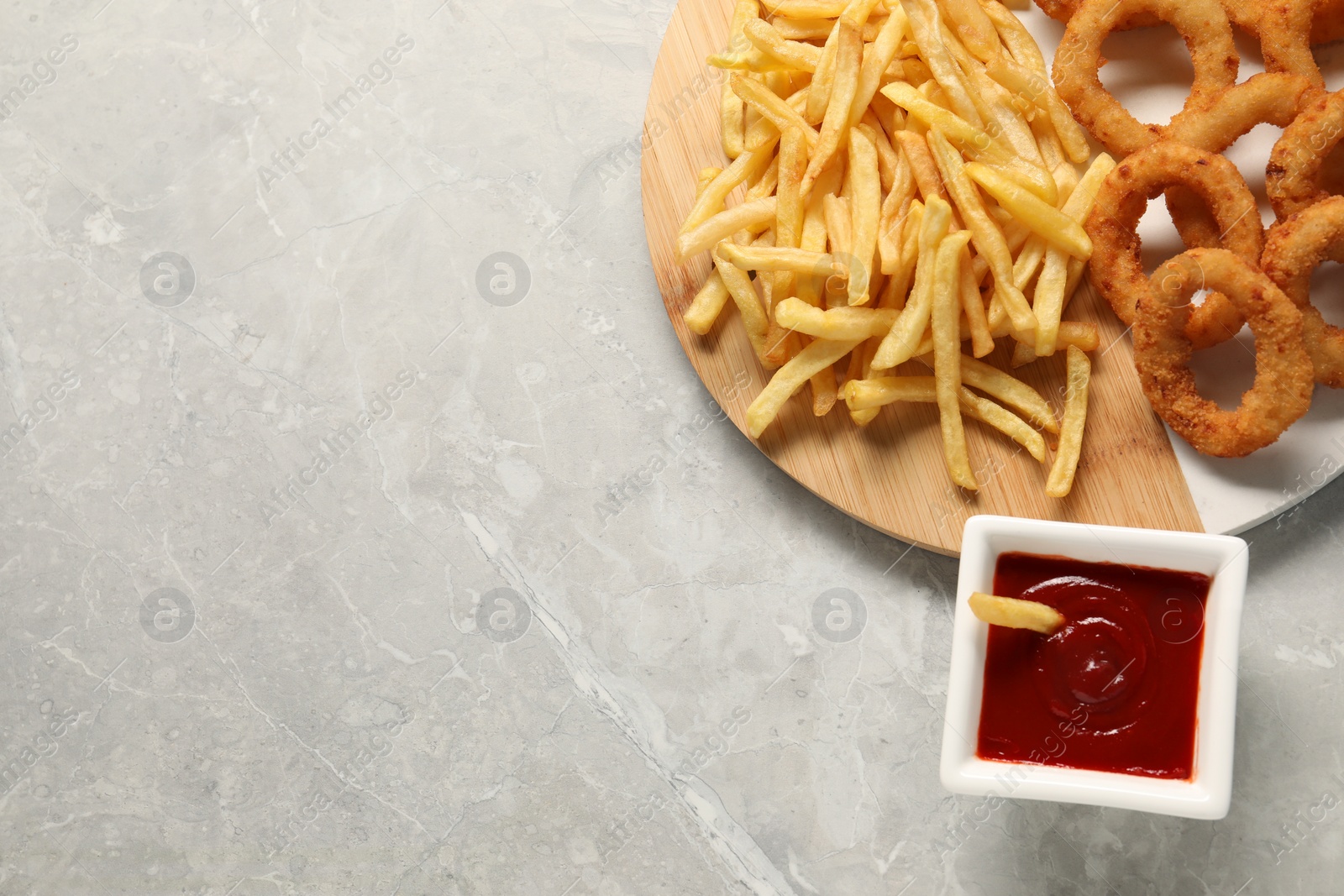 Photo of Tasty ketchup with fries and onion rings on grey marble table, flat lay. Space for text