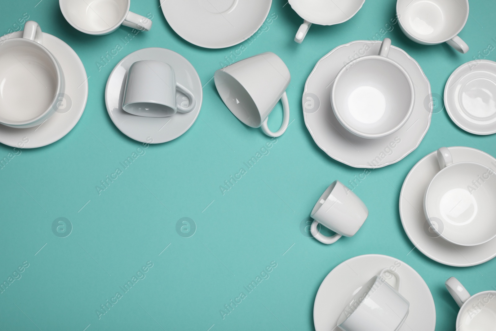 Photo of White cups and saucers on turquoise background, flat lay. Space for text