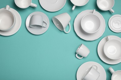 White cups and saucers on turquoise background, flat lay. Space for text