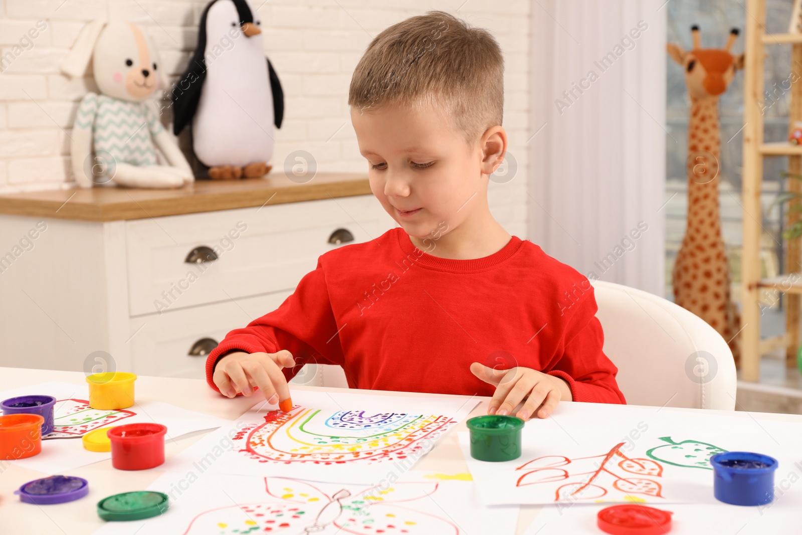 Photo of Little boy painting with finger at white table indoors