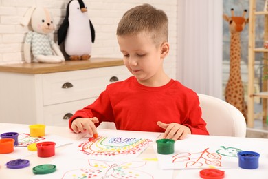Little boy painting with finger at white table indoors