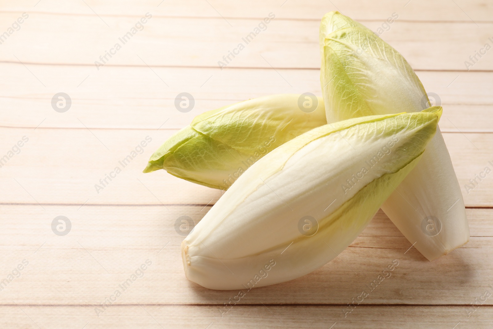 Photo of Raw chicories on wooden table, closeup. Space for text