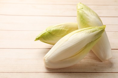 Photo of Raw chicories on wooden table, closeup. Space for text