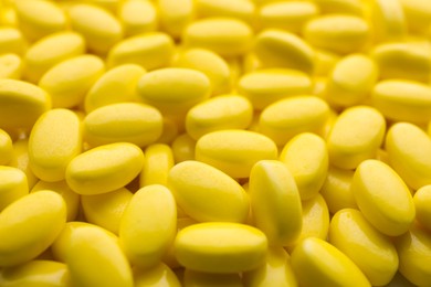 Photo of Pile of tasty yellow dragee candies as background, closeup