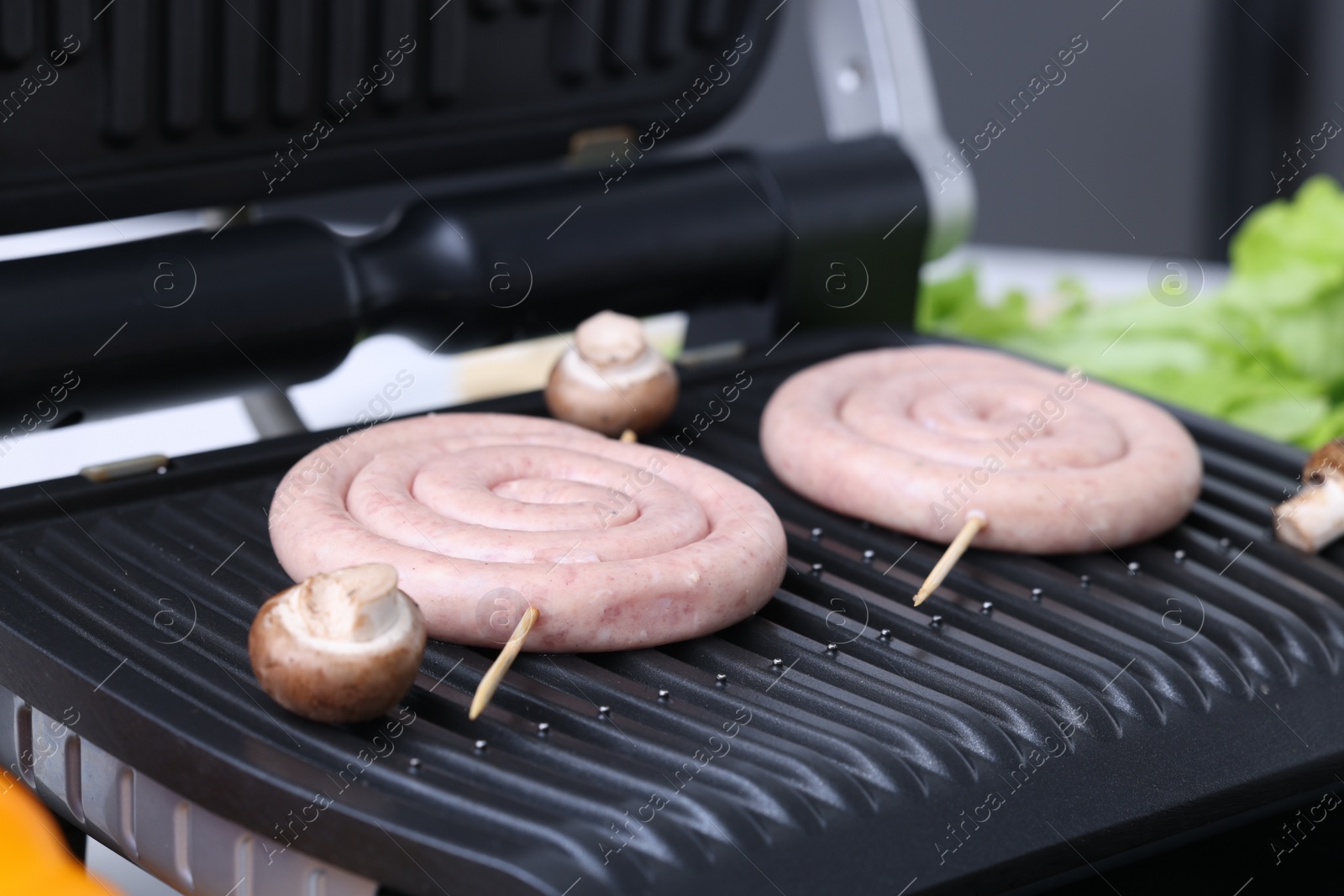 Photo of Electric grill with homemade sausages and mushrooms on table, closeup