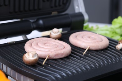 Electric grill with homemade sausages and mushrooms on table, closeup