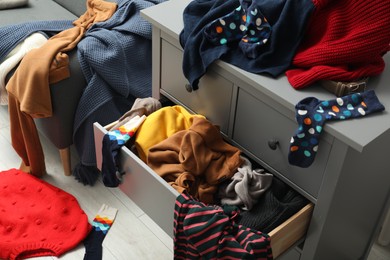 Cluttered chest of drawers indoors. Clothes in mess