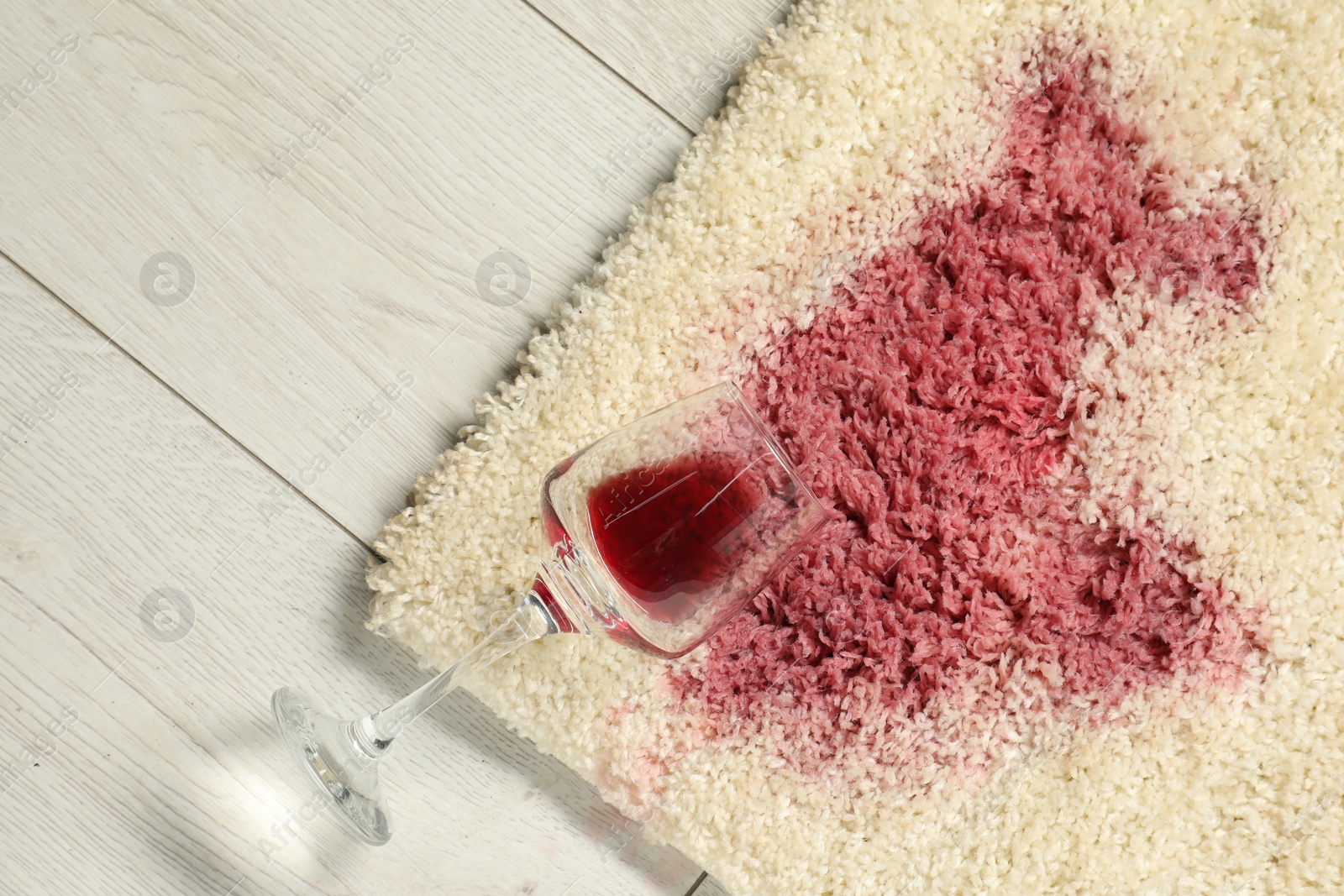 Photo of Overturned glass and spilled red wine on beige carpet, top view. Space for text