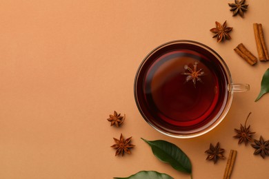 Photo of Cup of tea, anise stars, green leaves and cinnamon sticks on brown background, flat lay. Space for text