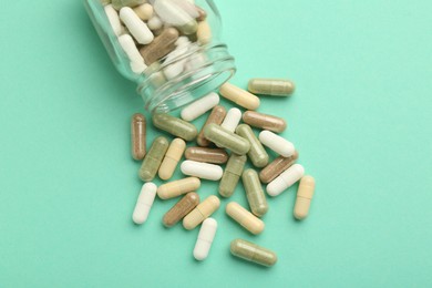 Photo of Vitamin pills and bottle on mint color background, top view