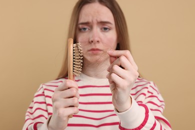 Photo of Woman untangling her lost hair from brush on beige background, selective focus. Alopecia problem