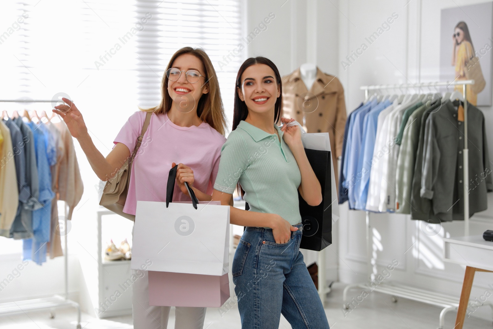 Photo of Young women with shopping bags choosing clothes in modern boutique