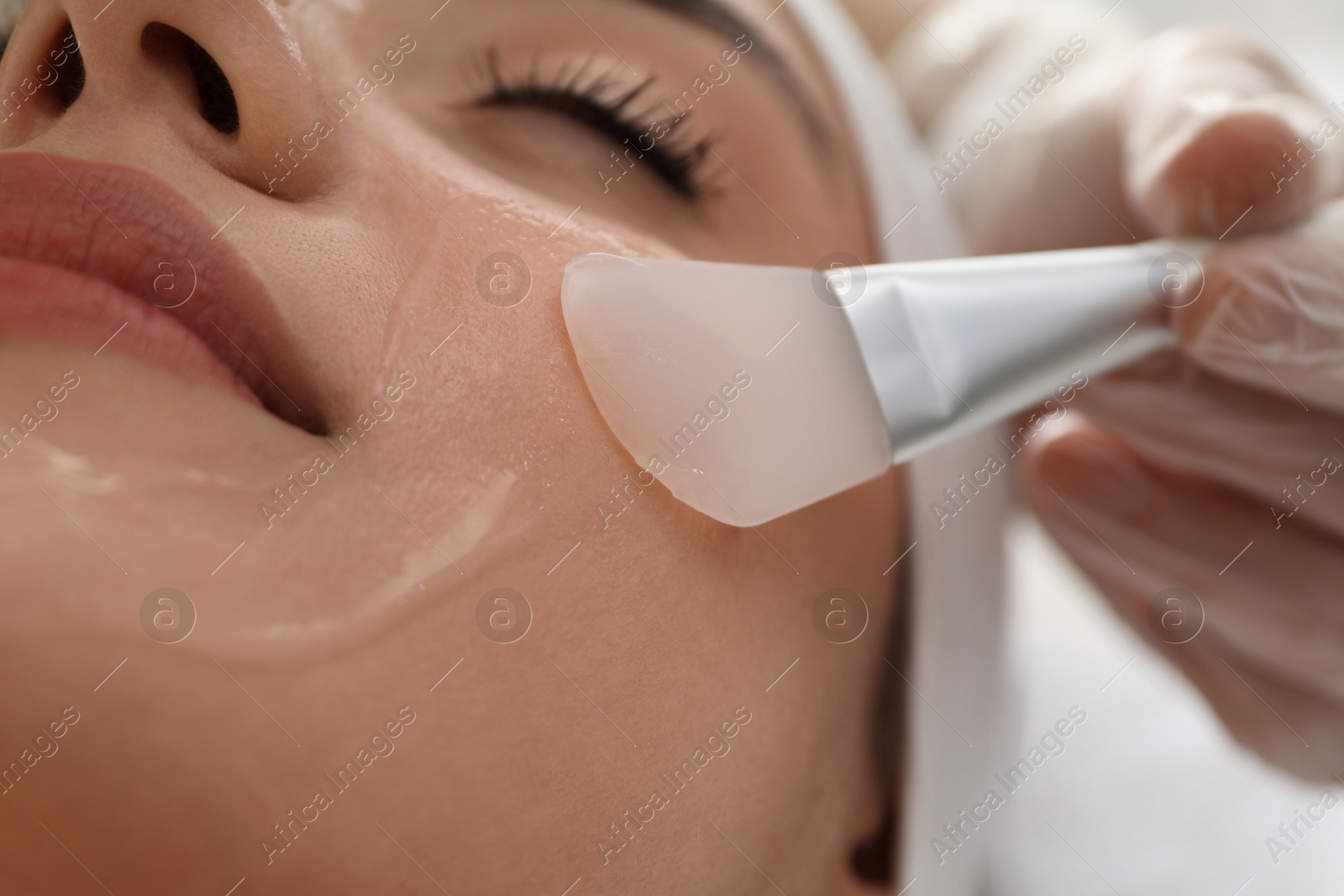 Photo of Young woman during face peeling procedure in salon, closeup