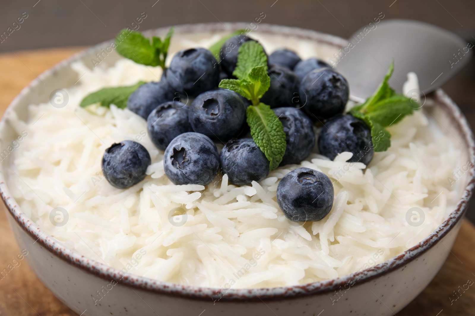 Photo of Bowl of delicious rice porridge with blueberries and mint on table, closeup