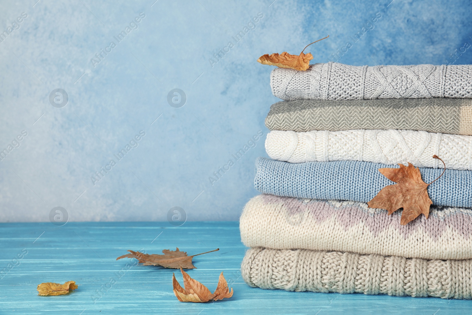 Photo of Stack of warm clothes with autumn leaves on table. Space for text