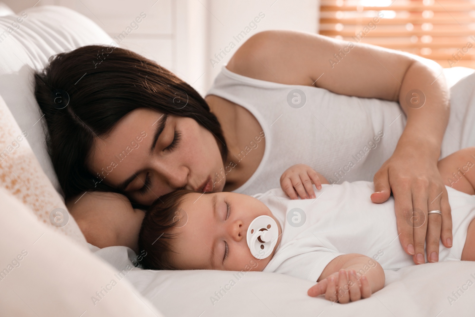 Photo of Young mother resting near her sleeping baby on bed at home