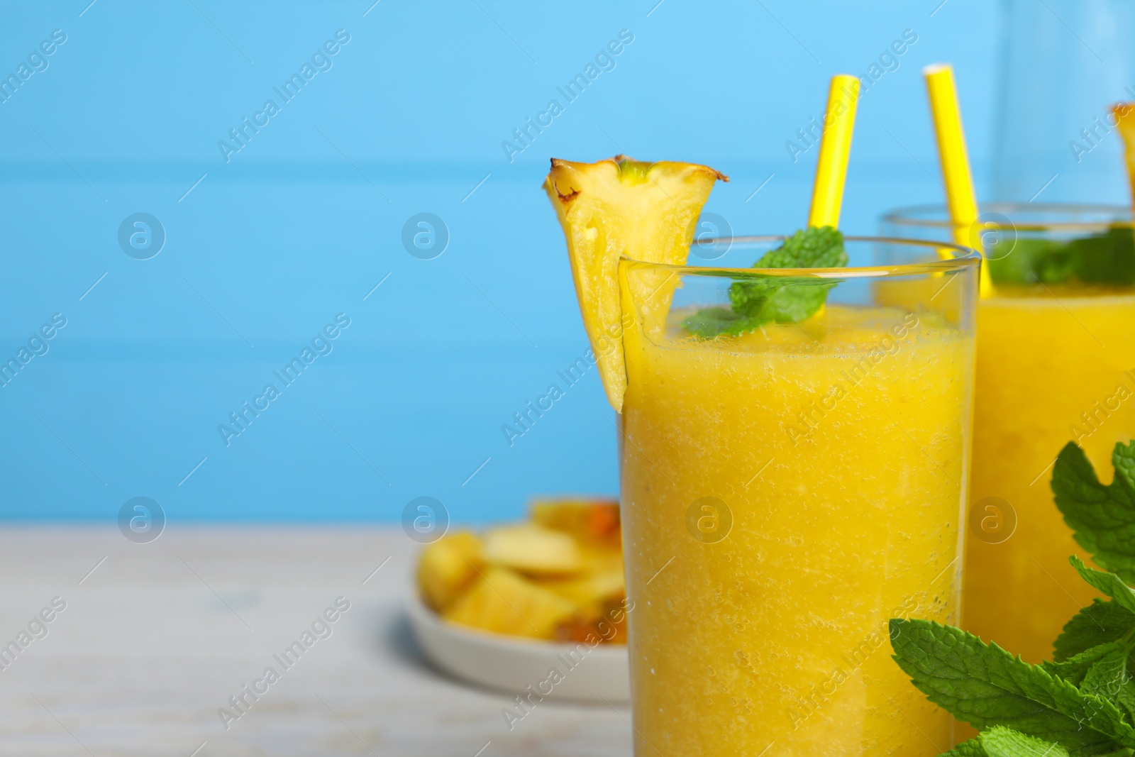 Photo of Tasty pineapple smoothie, mint and cut fruit on white table, closeup. Space for text