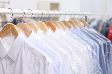 Photo of Dry-cleaning service. Many different clothes in plastic bags hanging on rack indoors, closeup