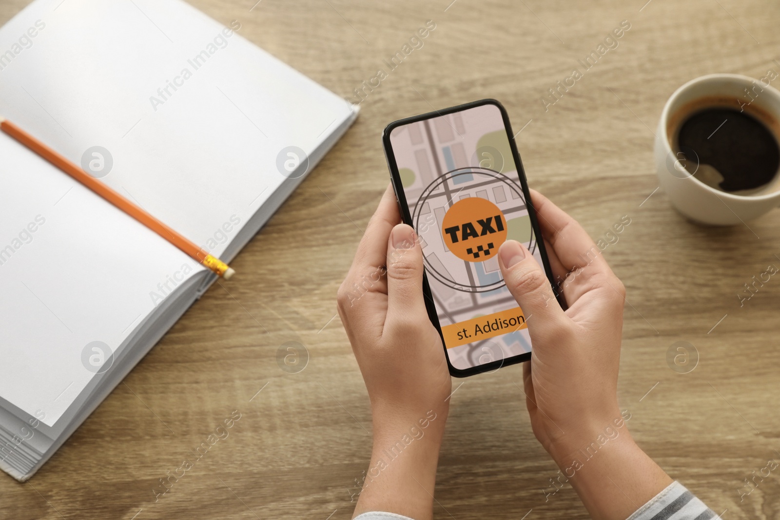 Photo of Woman ordering taxi with smartphone at wooden table, closeup