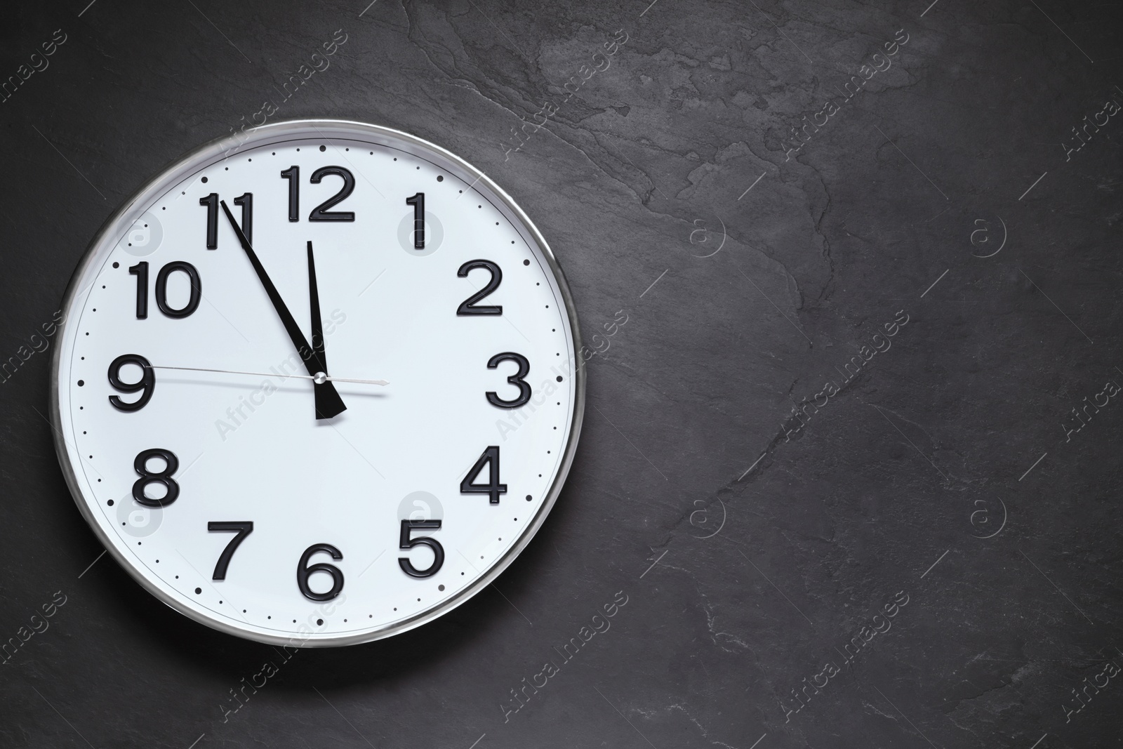 Photo of Clock showing five minutes until midnight on black table, top view with space for text. New Year countdown