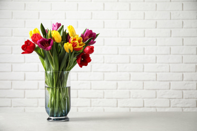 Photo of Beautiful spring tulips in vase on table near white brick wall. Space for text