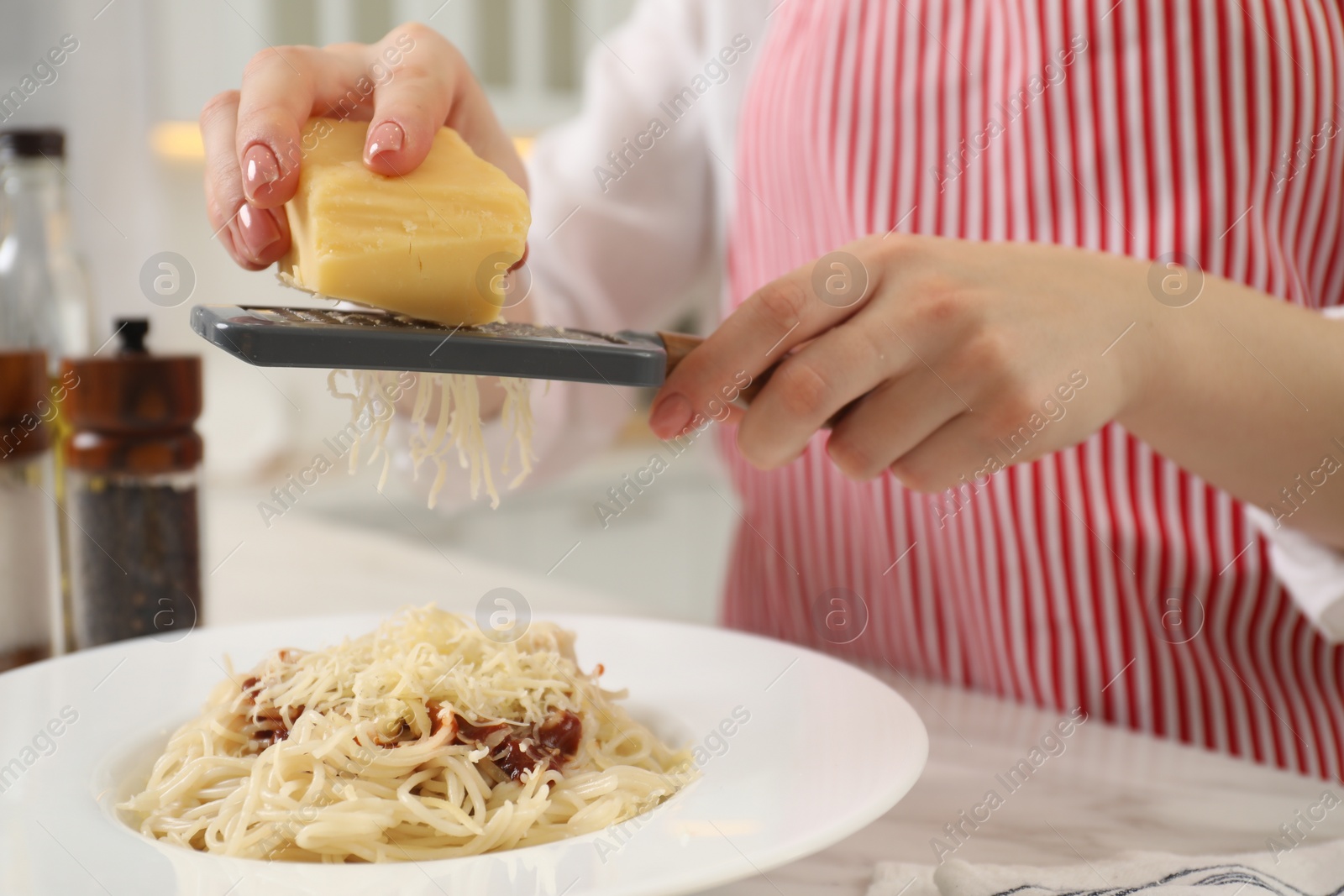 Photo of Woman grating cheese onto delicious pasta at white marble table in kitchen, closeup