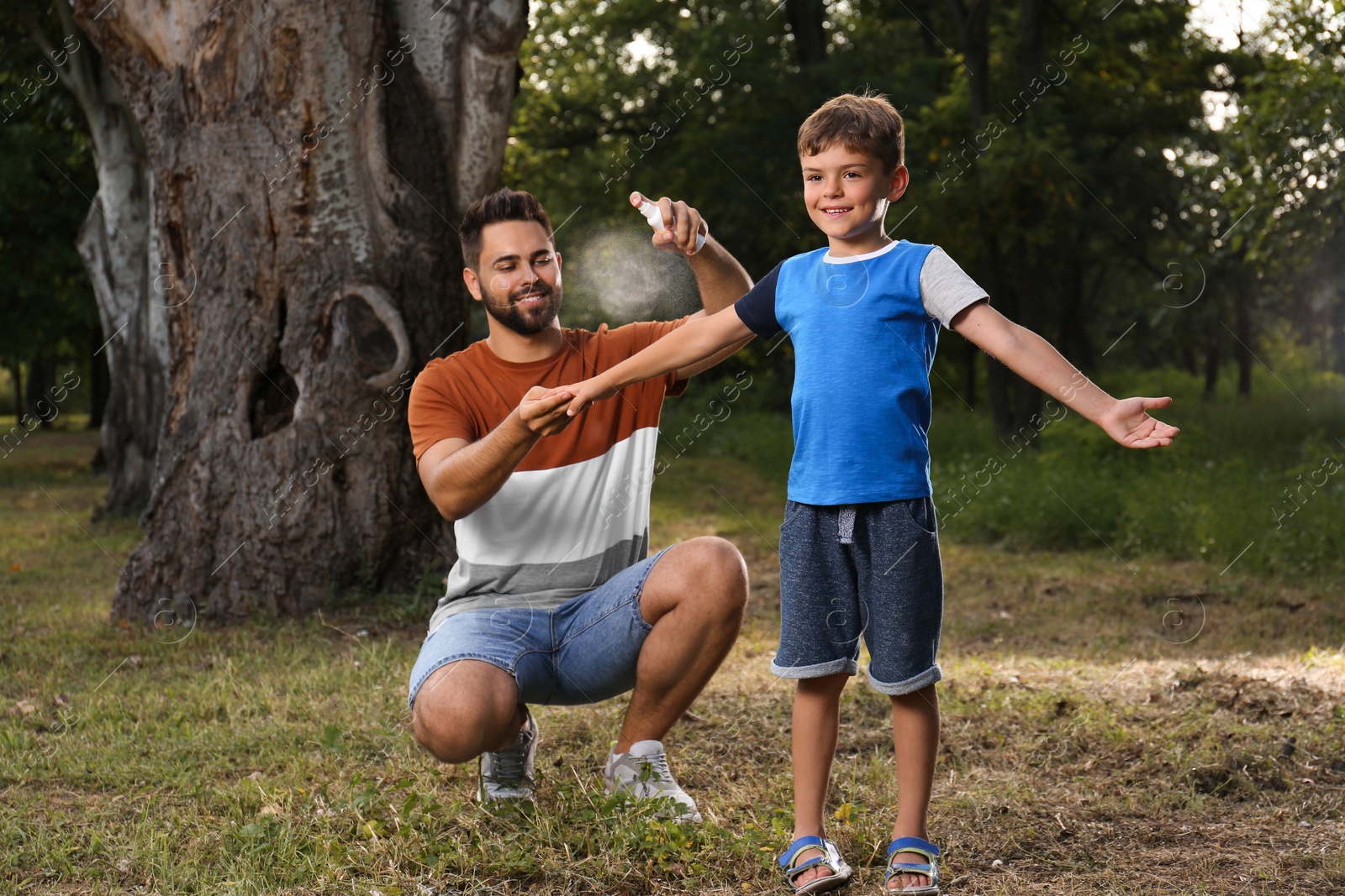 Photo of Man applying insect repellent on his son's arm in park. Tick bites prevention