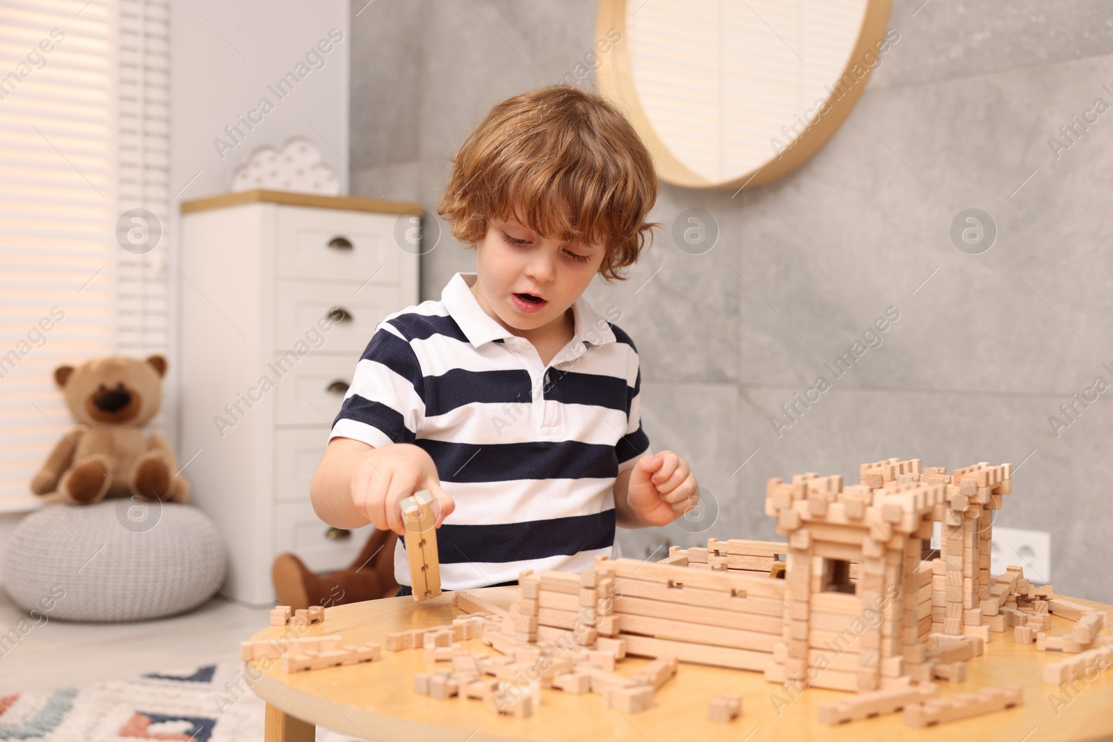 Photo of Little boy playing with wooden entry gate at table in room. Child's toy