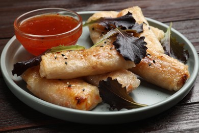 Tasty fried spring rolls, lettuce and sauce on wooden table, closeup